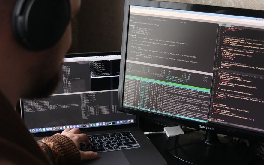 Programador revisando código en dos pantallas en un despacho en penumbra
